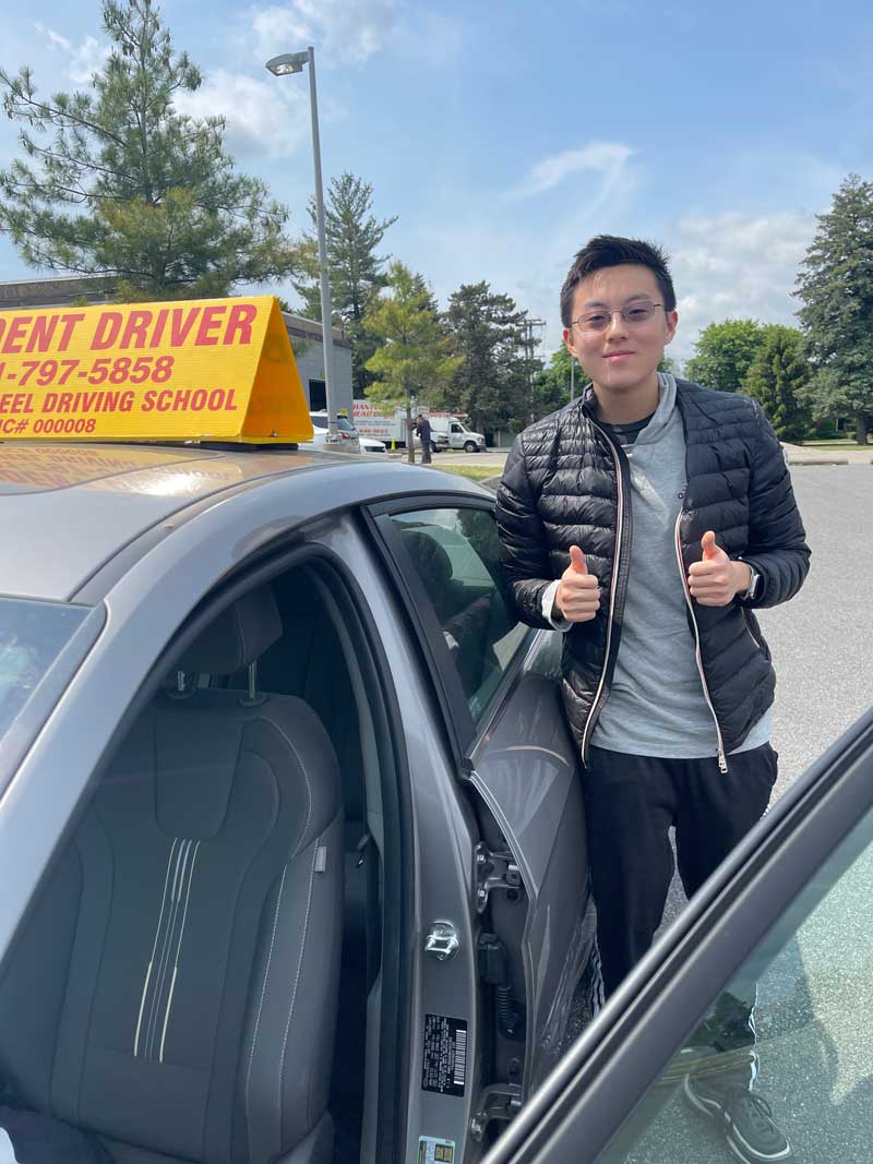 Student giving a thumbs up beside the Golden Wheel student-driver car